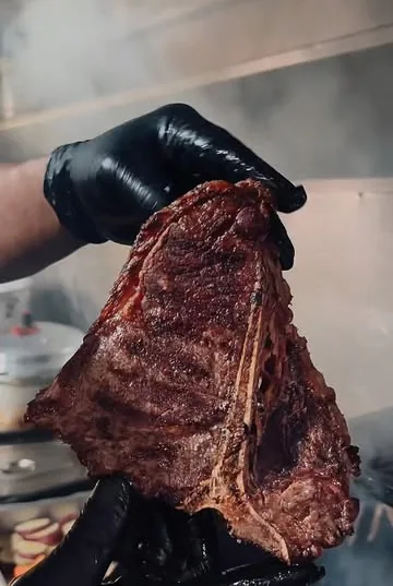 Corte de carne com osso segurado por mãos com luvas pretas